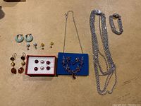 Photo showing all jewelry items arranged on a flat surface: multiple pairs of earrings on the left, two chain necklaces and a chunky bracelet on the right.