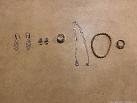 Top view of the full collection showing earrings, rings, bracelet, and necklace laid flat on a beige surface