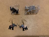 Two elephant brooches and one pair of elephant earrings shown together. Brooches are on top, one black enamel and one silver glitter. Earrings below are black enamel with colorful design.