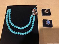 Full view of the turquoise bead necklace and two rings on black display pads, showing the jewelry arrangement and condition.