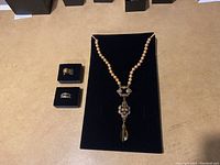 Full view of necklace on black display with two rings beside it on small black stands showing jewelry set