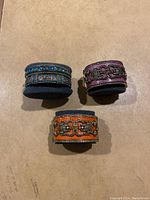 Three metal cuff bracelets on foam mounts: blue, purple, and orange