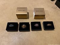 Overview of four rings displayed on black velvet platforms with two gold Heidi Daus boxes behind them.