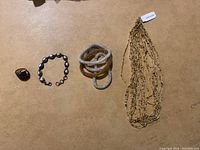 Four pieces of Himalayan jewelry: a dark stone ring, a silver-tone ring with red stones, a pearl-like bead bracelet, a cream-colored coil bracelet, and a multi-strand beaded necklace.