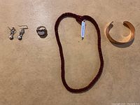 Full view of all four jewelry items on a beige surface showing the necklace, bracelet, ring, and earrings.