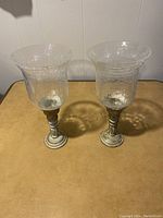 Pair of large decorative candle holders, clear textured glass shades with metal bases in a distressed silver finish.