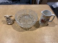 Full lot view showing glass bowl, angel figurine, and floral ceramic cream pitcher on table.