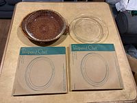 The lot items arranged on a table showing two glass pie plates, a wicker holder, and two Pampered Chef pie crust shields in packaging.