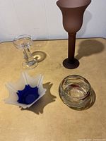 Four assorted candle holders on a beige surface against a white wall.