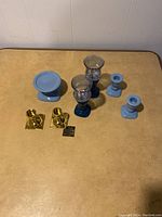Photo showing all seven candle holders including two brass, three blue ceramic, and two blue glass holders on a yellow surface