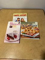 Three cookbooks on a table - Crazy Plates, The Big Book of Chocolate 365, The New Taste of Home Appetizer