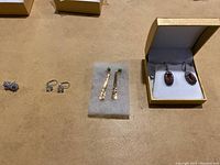 Four pairs of earrings arranged side by side on a tan surface, with one pair in a display box.