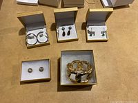 Five jewelry pieces in boxes on table including four pairs of earrings and one bracelet
