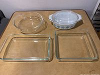 Four Pyrex dishes displayed on table: two rectangular clear glass dishes, one round clear glass dish, one white round casserole dish with blue snowflake pattern.