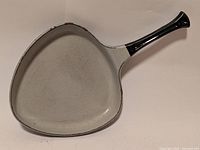 Top view of the triangular-shaped enamel frying pan showing the light gray cooking surface and black handle.