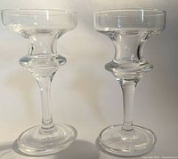 Two clear glass footed candlesticks shown together with symmetrical shape and polished crystal clear glass finish.