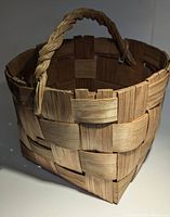 Front angled view of a rustic handmade basket showing woven wooden strips and braided handle.