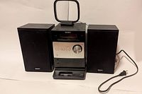 Front view of Sony micro hi-fi system with iPod dock and two speakers side by side showing overall system and power cord