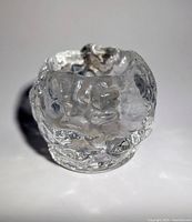 Close-up image of a clear textured glass candle holder with an organic, uneven surface resembling a snowball
