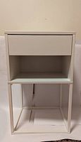 Front view of white nightstand with drawer and open shelf, metal legs visible.