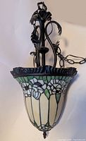 Overall view of pendant lamp showing stained glass floral shade and metal chain with leaf motifs
