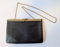Front view of the black embossed lizard texture purse with gold chain strap laid flat.