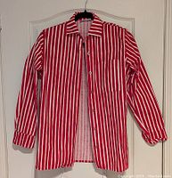 Front view of red and white striped long sleeve shirt hanging on black hanger against white door.