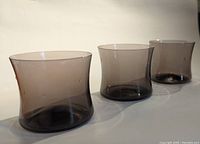 Photo showing three smoked glass drinking glasses arranged in a row with visible smoke tint and curved shape.