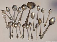 Photo of a collection of 17 assorted souvenir and decorative spoons arranged on a neutral background.