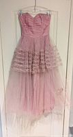 Full view of vintage 1950s pink strapless prom dress hanging on hanger, showing fitted ruched bodice and long multi-layered tulle skirt with ruffles.