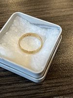 Close-up image of plain gold band ring in a small white cushioned box, showing interior stamp '10K'