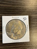 Obverse side of a 1974 US Eisenhower dollar coin mounted in cardboard holder showing profile of Eisenhower and inscriptions.