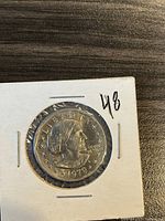 Obverse side of 1979 Susan B Anthony dollar coin showing Susan B Anthony portrait, year 1979, and 'LIBERTY'. Coin in a white cardboard holder with number '48'.