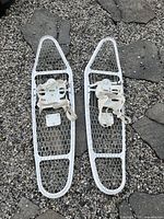 Pair of white army snow shoes showing metal frame, mesh netting, and adjustable bindings on top surface