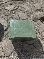 Closed view of green storage box on stone and gravel ground showing scratches and condition.