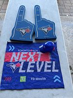 Photo of two blue foam hands with Blue Jays logo, a blue break-apart piggy bank, and a rally towel with 'Next Level' text and TD Wealth logo