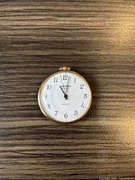 Front view of the Cardinal pocket watch showing white dial, black numerals, and gold-toned crown.