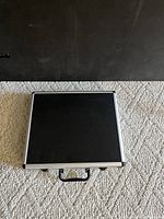 Closed black aluminum carrying case for the cleaning kit photographed on carpeted floor