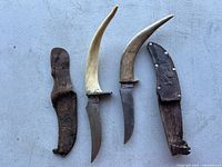 Photo of two vintage hunting knives with curved handles and two leather sheaths on a grey surface.