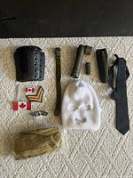Overview of assorted military items laid out on carpet including arm guard, belts, flashlight, necktie, balaclava, patches, and badges