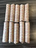 Photo displays 10 unopened paper rolls of pennies arranged in two neat rows on a wood surface