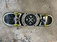 Top view of the skateboard showcasing the black deck with white border and RWLD logo, yellow wheels, and trucks on concrete floor.
