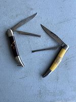 Two vintage fish cutters, one with a dark handle and the other yellow, both with multiple folding tools including blades and serrated edges.