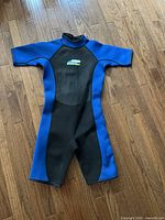 Full view of the short sleeve blue and black wet suit laid flat on wood flooring showing the front side.