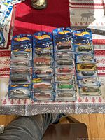 24 unopened Hot Wheels cars laid out on table, five columns of four to five cars each, showcasing original packaging with colorful vehicle illustrations.