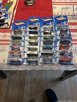 Overview of 27 unopened Hot Wheels cars displayed in blister packaging on a table, showing a variety of car styles and colors.