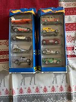 Two unopened Hot Wheels gift packs from 2000 era on a patterned red and white surface