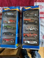 Two unopened Hot Wheels gift packs each with five die-cast cars, showing the full contents and packaging