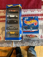 Photo showing the Hot Wheels gift pack with five diecast cars in packaging and the single Hot Wheels 2000 First Editions Ferrari 333 SP car packaging to the right on a fabric background.