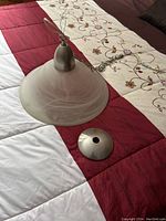 Front view of the kitchen light fixture showing the frosted glass shade with swirl pattern and metal mount plate and wiring chain.